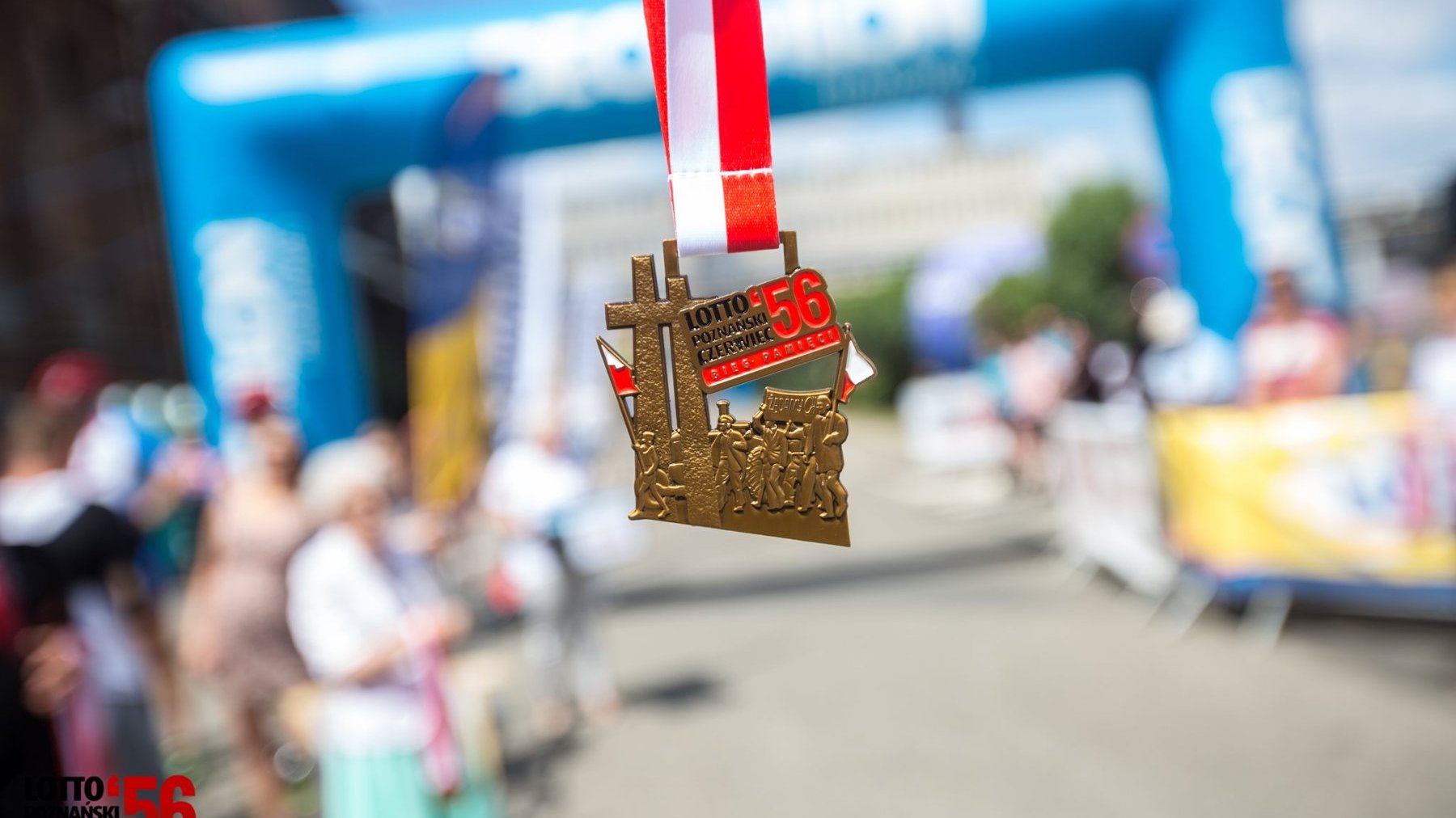 Medal z okazji Biegu Pamięci Poznańskiego Czerwca '56. W tle meta trasy i kibice, którzy stoją przy barierkach.