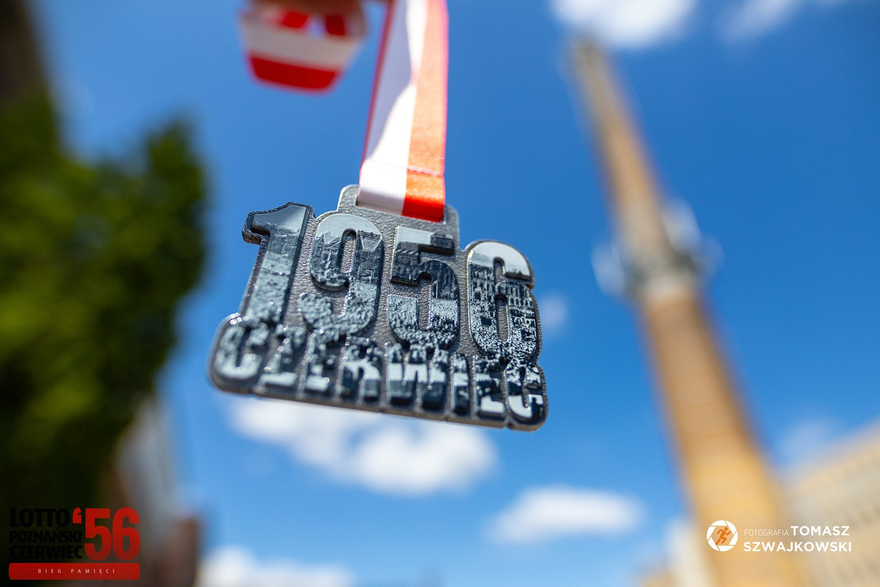 Zwisający medal z napisem "1956 Czerwiec". W tle wysoki komin hutniczy. - grafika artykułu