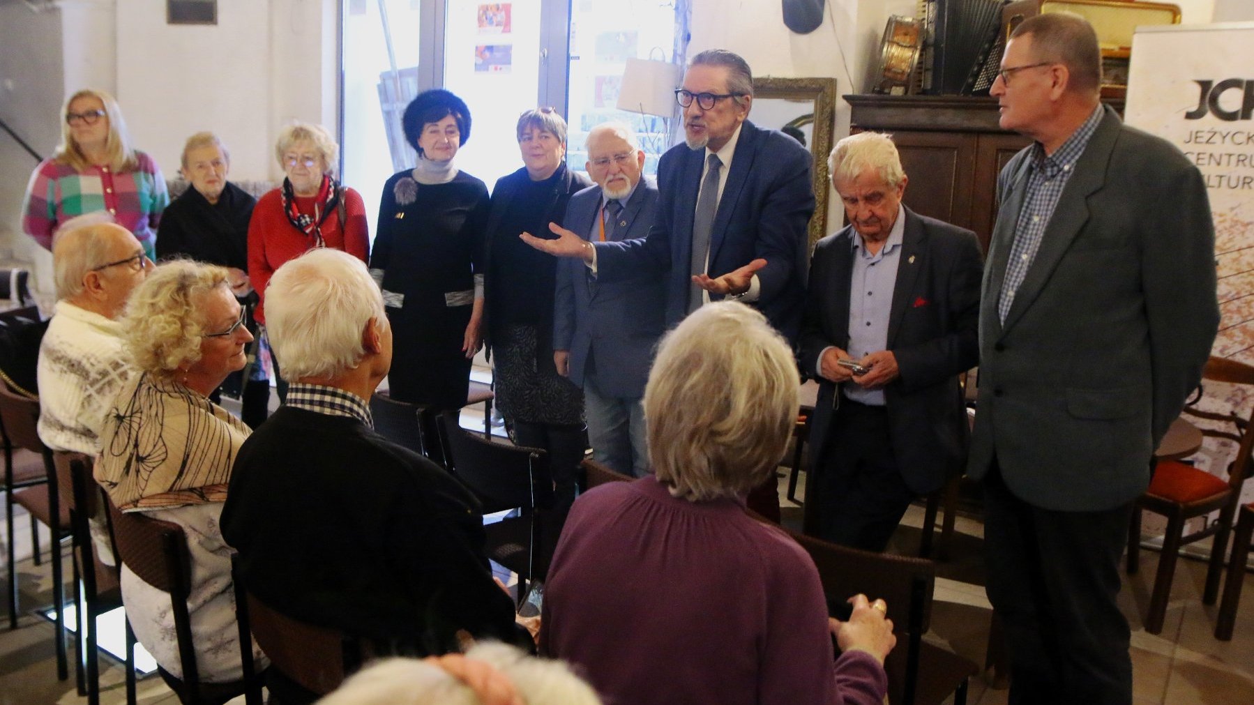 Zdjęcie przedstawia Miejską Radę Seniorów oraz seniorów z Jeżyc podczas spotkania w JCK w trakcie rozmowy.