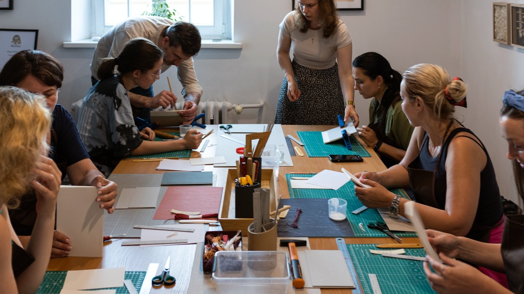 Zdjęcie przedstawia warsztaty introligatorskie, w trakcie których uczestnicy własnoręcznie szyją notesy