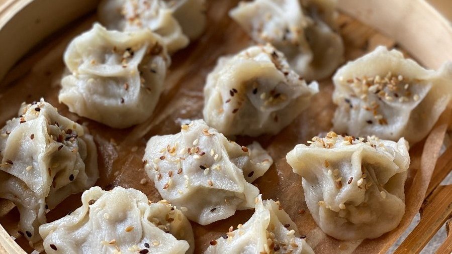 Azjatyckie pierożki w cienkim cieśnie, posypane sezamem. Leżą na bambusowej tacce.