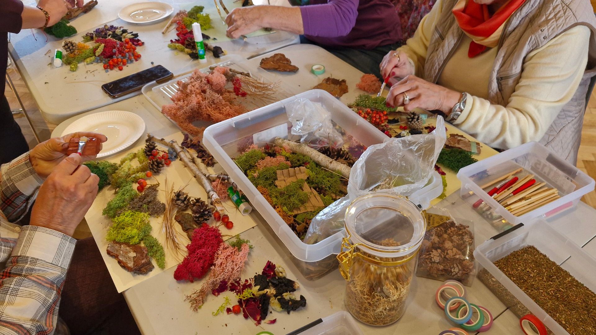 4. Na zdjęciu przedstawiona jest część warsztatowa, w której seniorzy tworzą swoje kompozycje za pomocą naturalnych materiałów jak: szyszki, mech, igliwie, trawy, płatki kwiatów, kora itp., angażując również inne zmysły zapoznając się z ich różnymi fakturami, kolorem, czy zapachem.