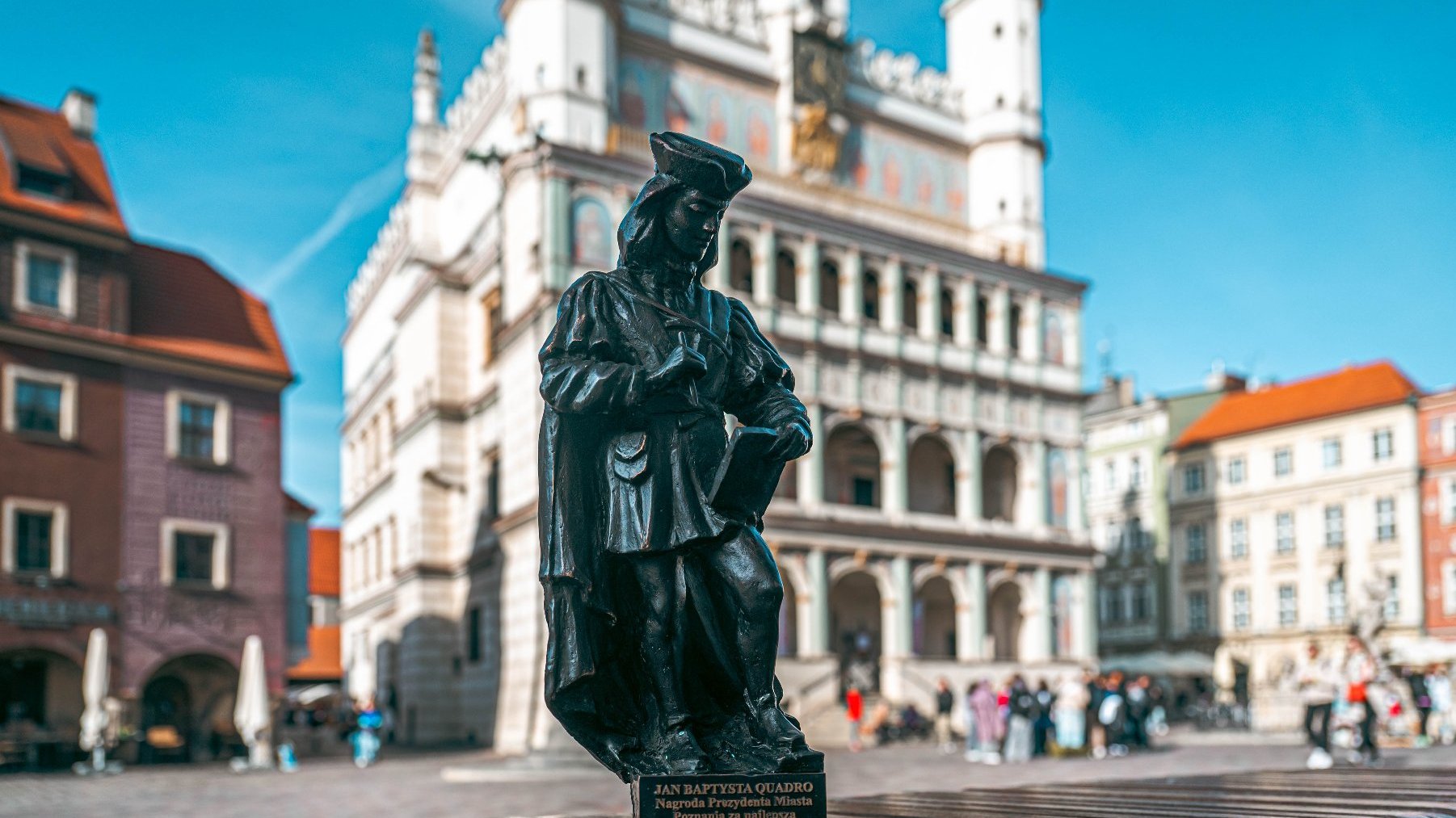 Zdjęcie przedstawia statuetkę z podobizną Jana Baptysty Quadro na tle Ratusza.