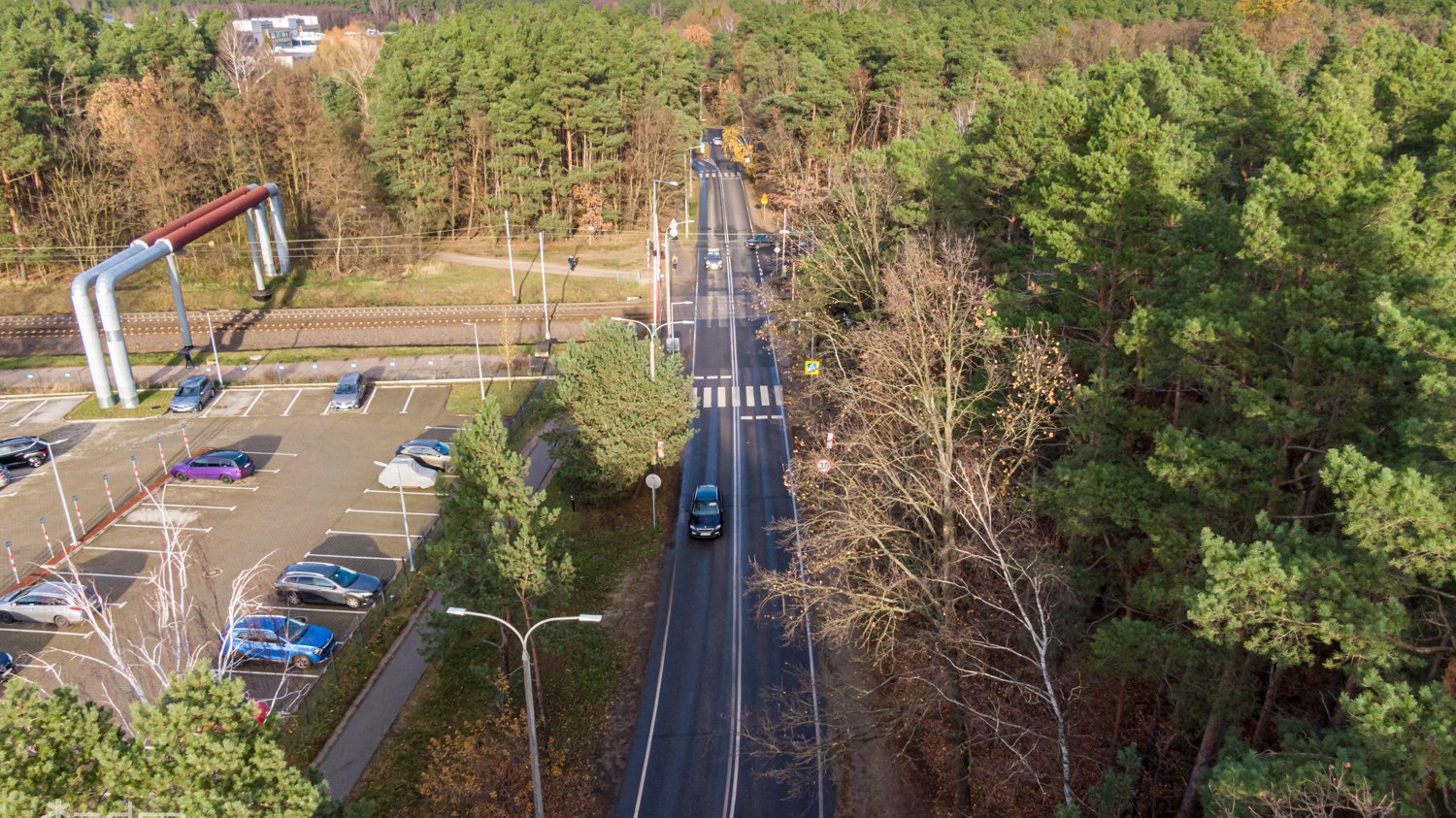 Widok z lotu ptaka na ul. Umultowską i samochody przejeżdżające przez przejazd kolejowy. Po lewej Las Żurawiniec, po prawej parking przy os. Batorego