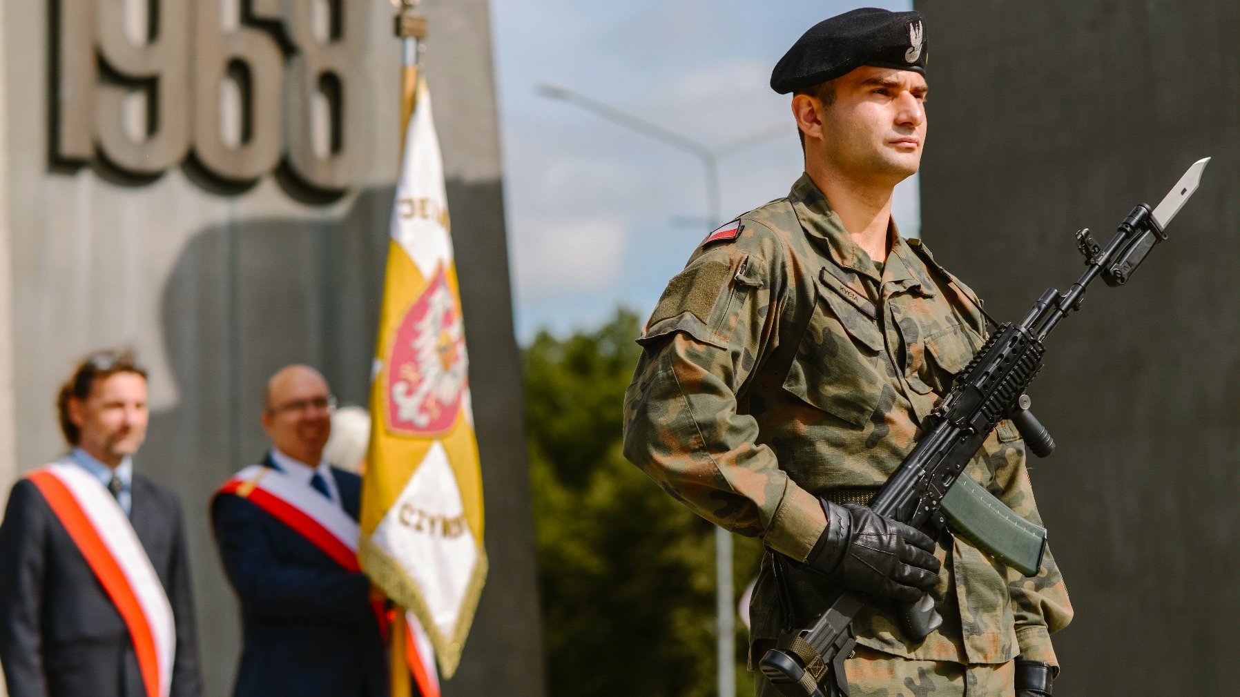 Zdjęcie przedstawia mężczyznę w mundurze pod pomnikiem.