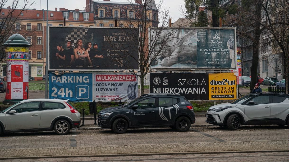 Reklamy na billboardach wzdłuż płotu na parkingu tymczasowym na placu Wiosny Ludów