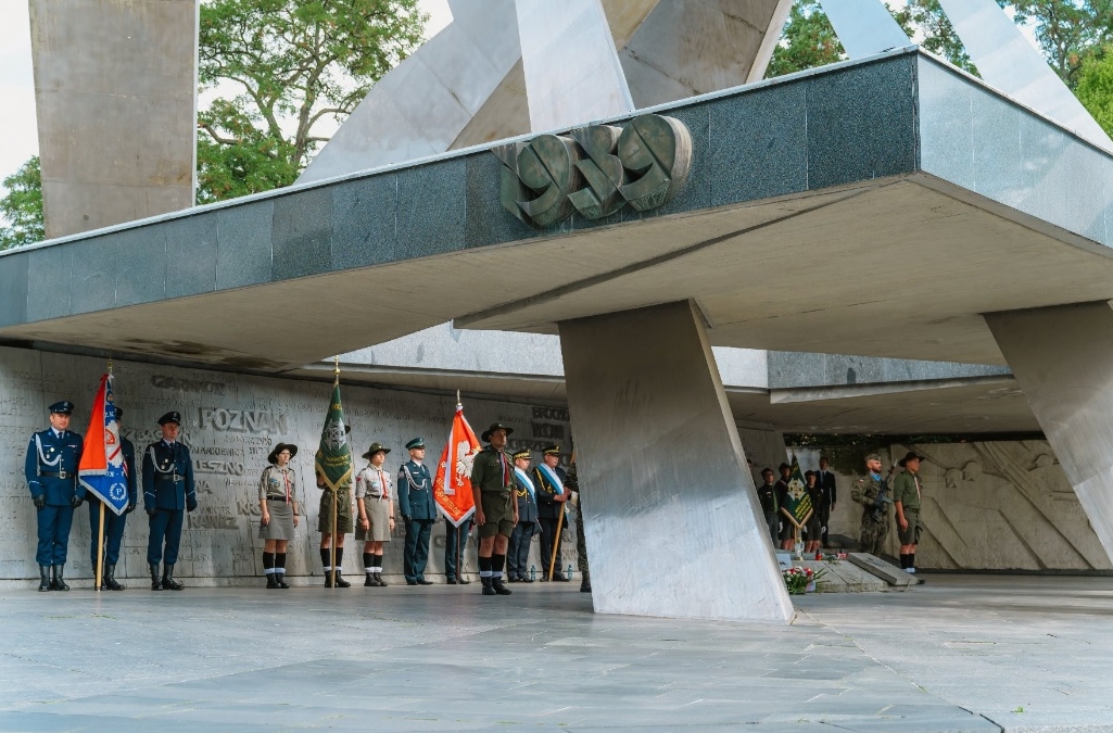 marmurowy pomnik o dużych rozmiarach, przy nim grupa osób w mundurach wojskowych i harcerskich, trzymają sztandary - grafika artykułu