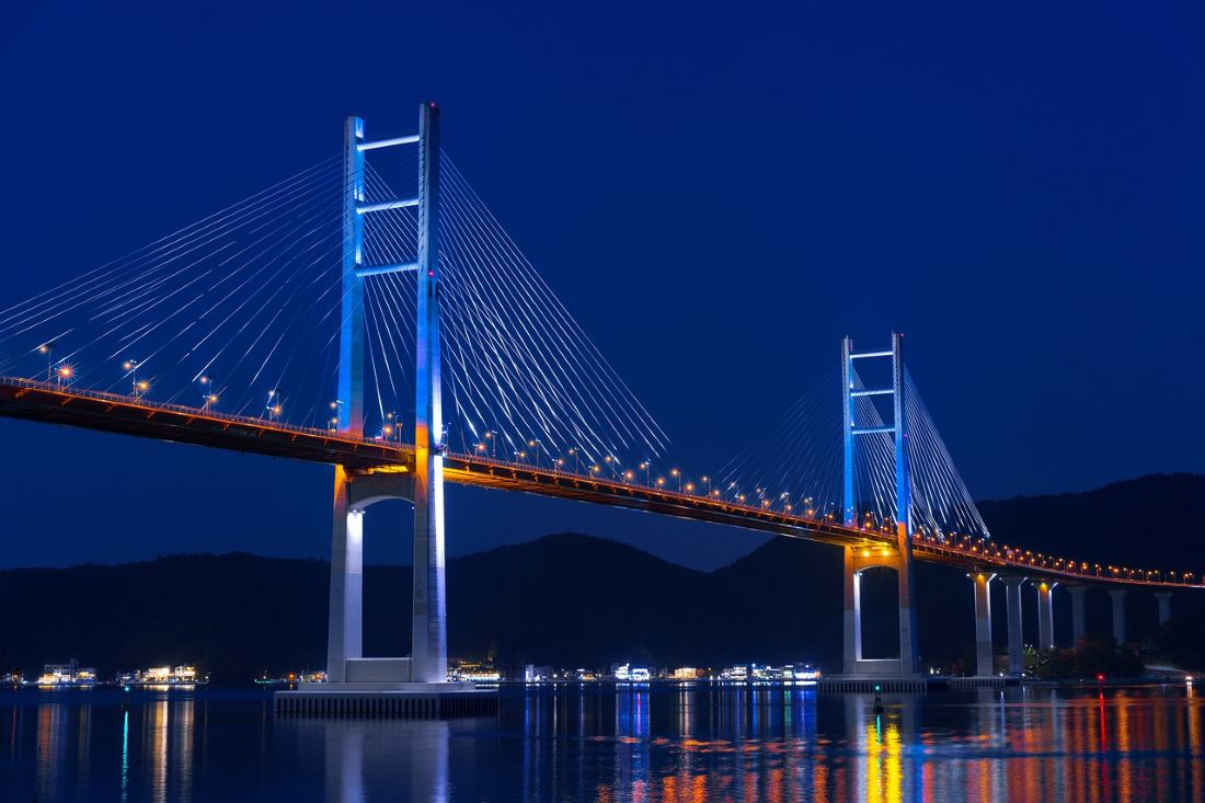 most o dwóch wysokich przęsłach, nad wodą, podświetlony, światła odbijają się w wodzie - grafika artykułu