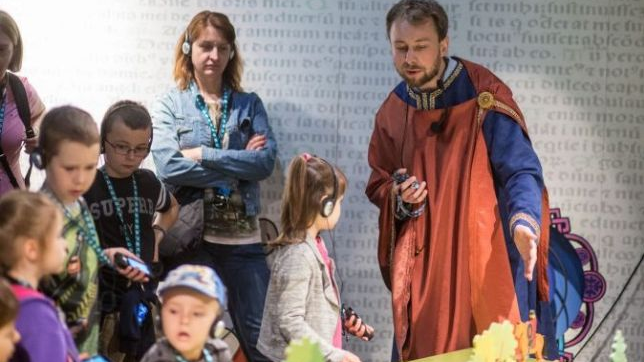 Dzieci słuchają przewodnika muzealnego przebranego w strój z epoki Mieszka I.