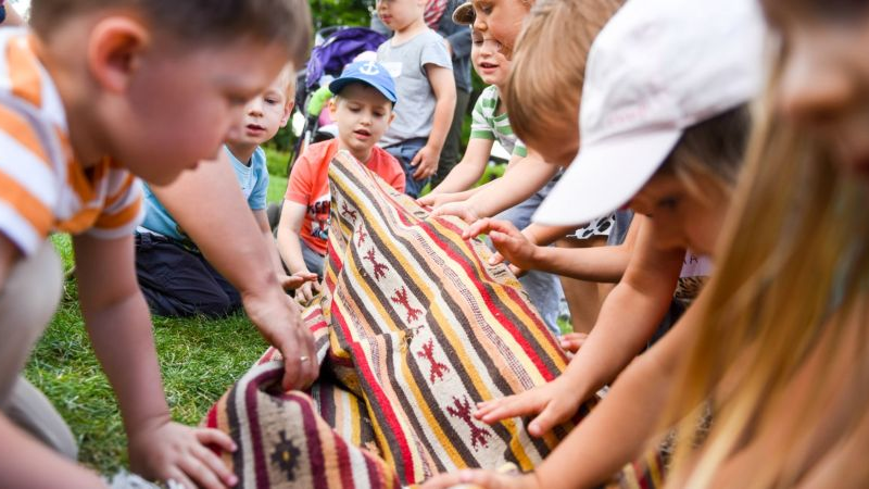 Grupa dzieci bawi się na trawie rozwijając kolorowy dywan.