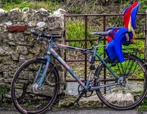Rodzinne wycieczki rowerowe to nie tylko świetny sposób na aktywne spędzanie czasu, ale również budowanie wspólnych wspomnień, fot. Pixabay Rower z zamontowanym fotelikiem rowerowym, oparty o kamienny mur, obok metalowa furtka.