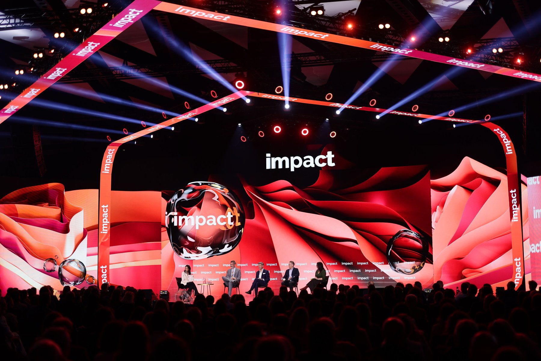 Znamy już szczegółową agendę Impact'25, który odbędzie się 14 i 15 maja w Poznaniu Scena konferencyjna z dużym ekranem wyświetlającym wielokrotnie słowo "impact". Na scenie pięć osób siedzących na krzesłach, prawdopodobnie uczestniczących w panelu dyskusyjnym. Tło w odcieniach czerwieni i pomarańczu, kilka kulistych obiektów także z napisem "impact". Dynamiczne oświetlenie skierowane na scenę, w tle widoczna publiczność