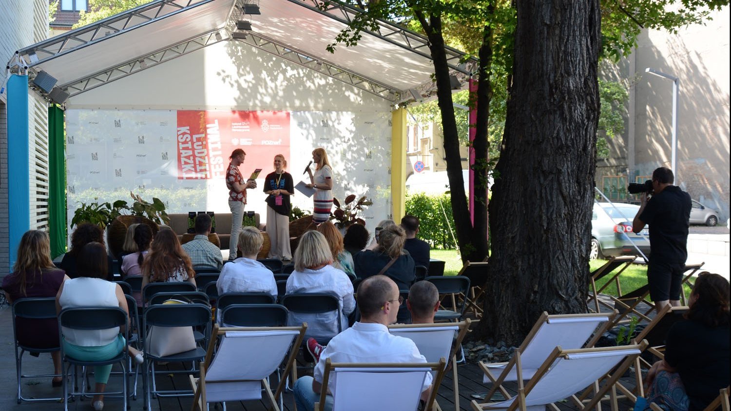 Zdjęcie przedstawia ludzi na scenie i przed sceną, siedzących na leżakach.