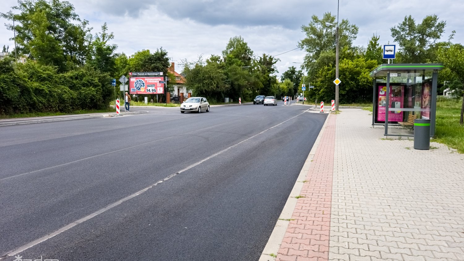 Zdjęcie przedstawia jezdnię, po której jeżdżą samochody oraz przystanek autobusowy.