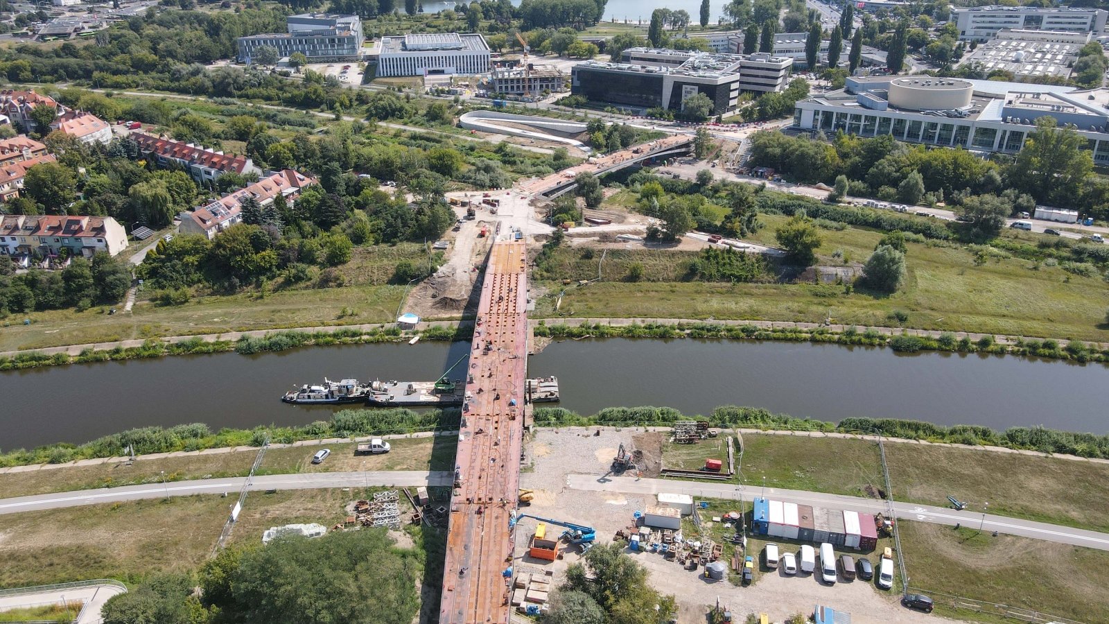 Zdjęcie przedstawia budowane mosty nad rzeką i otaczające budynki widziane z lotu ptaka.