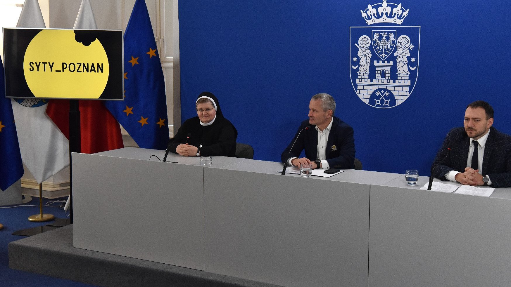 Na zdjeciu trzy osoby za stołem konferencyjnym, dwóch mężczyzn i zakonnica