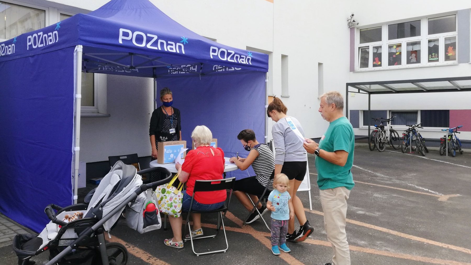 Grupa osób przy niebieskim stoisku na szkolnym patio.