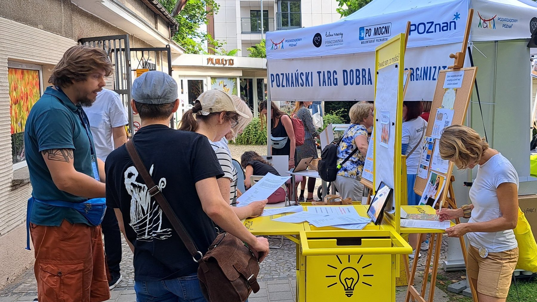 Grupa osób stoi przy straganach podczas Targu Dobra w Starym Zoo.