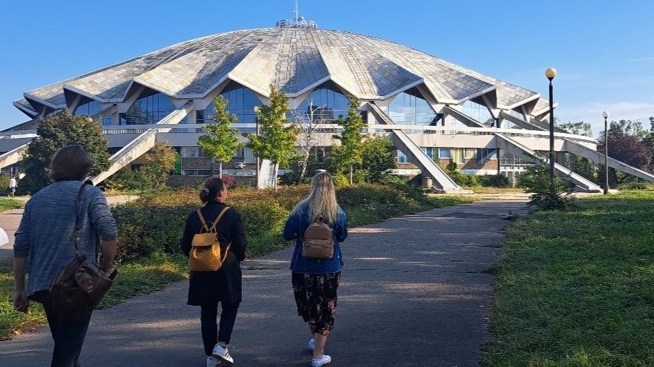 Grtupa osób spaceruje przed halą widowiskową Arena.