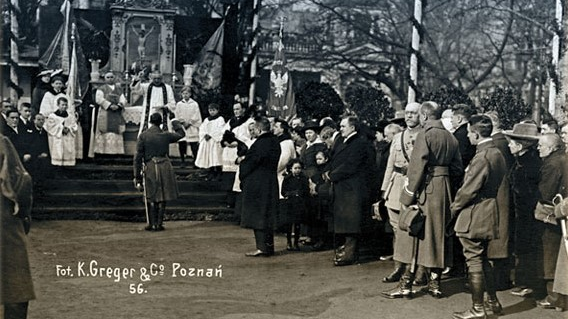 Zołnierze i cywile stojący przed ołtarzem polowym, przy którym stoją duchowni katoliccy.