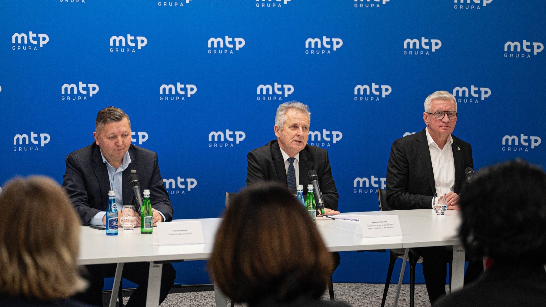 Na zdjeciu trzej męzczyźni za stołem konferencyjnym, za nimi ścianka z napisem: grupa mtp