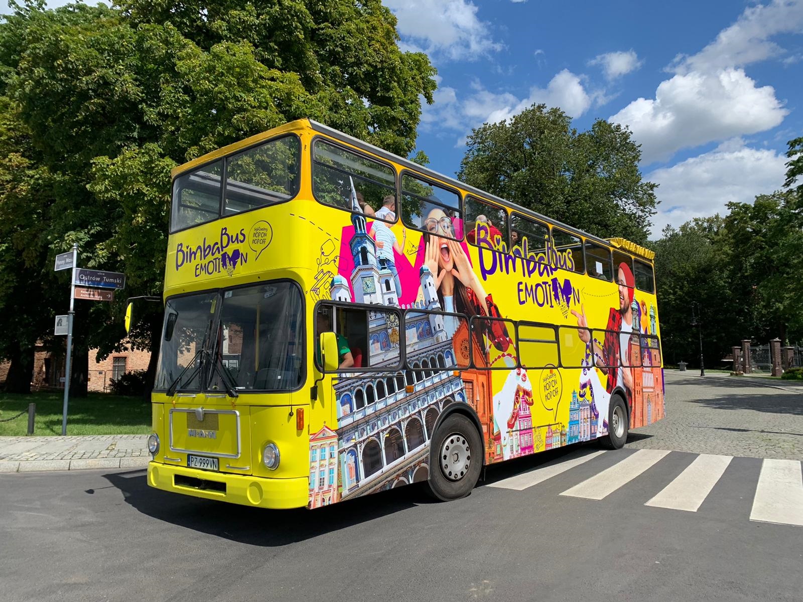 Na zdjęciu znajduje się żółty, turystyczny autobus, typu londyńskiego, jadący ulicą - grafika artykułu