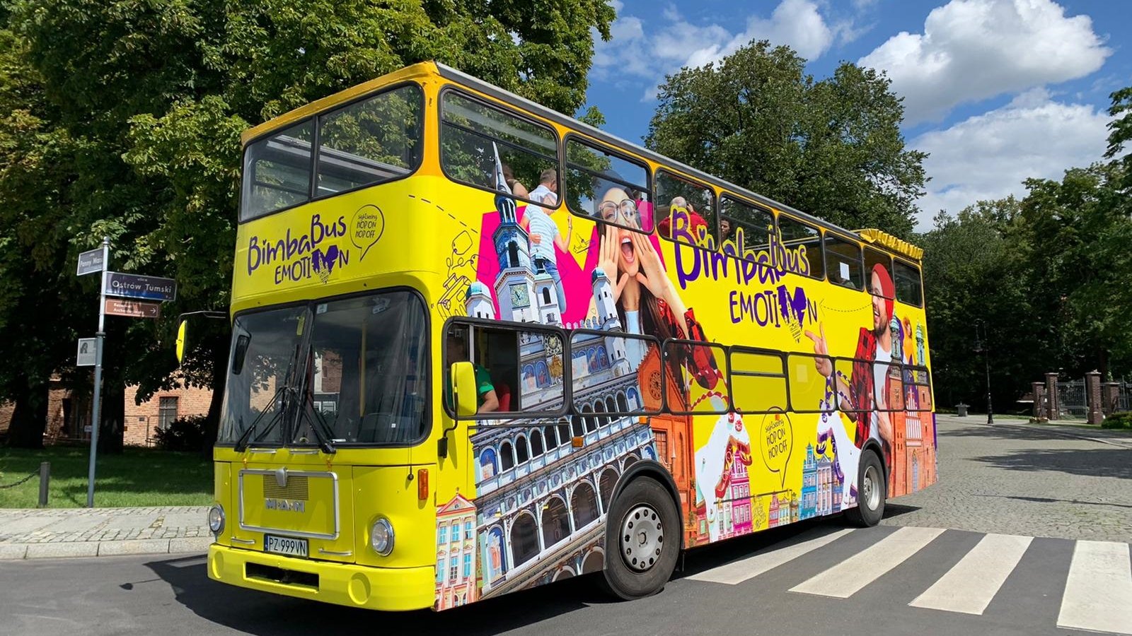 Na zdjęciu znajduje się żółty, turystyczny autobus, typu londyńskiego, jadący ulicą