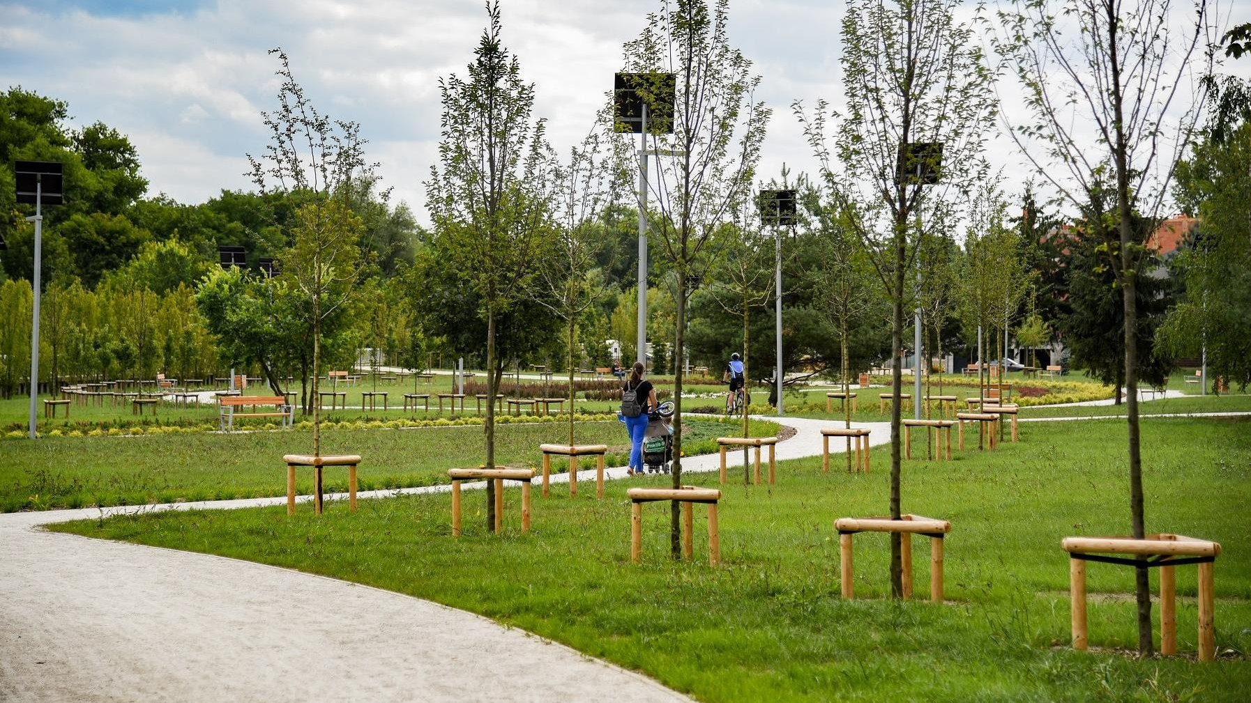 Na zdjęciu znajduje się zadbany park z alejkami spacerowymi, po których chodzą ludzie