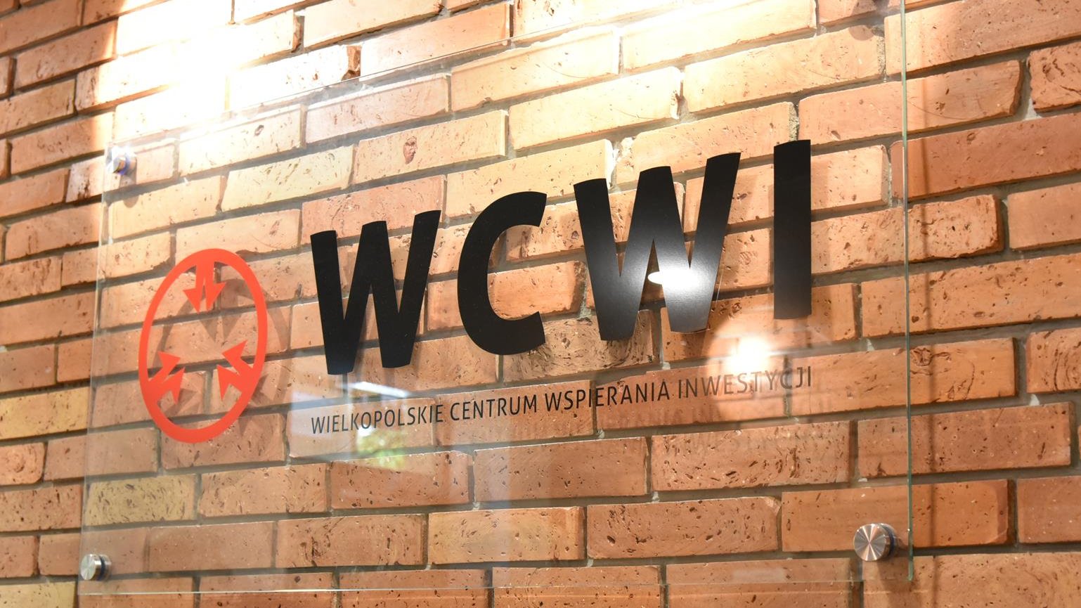 Zdjęcie przedstawia napis "WCWI" na szybie, wiszącej na ceglanej ścianie.