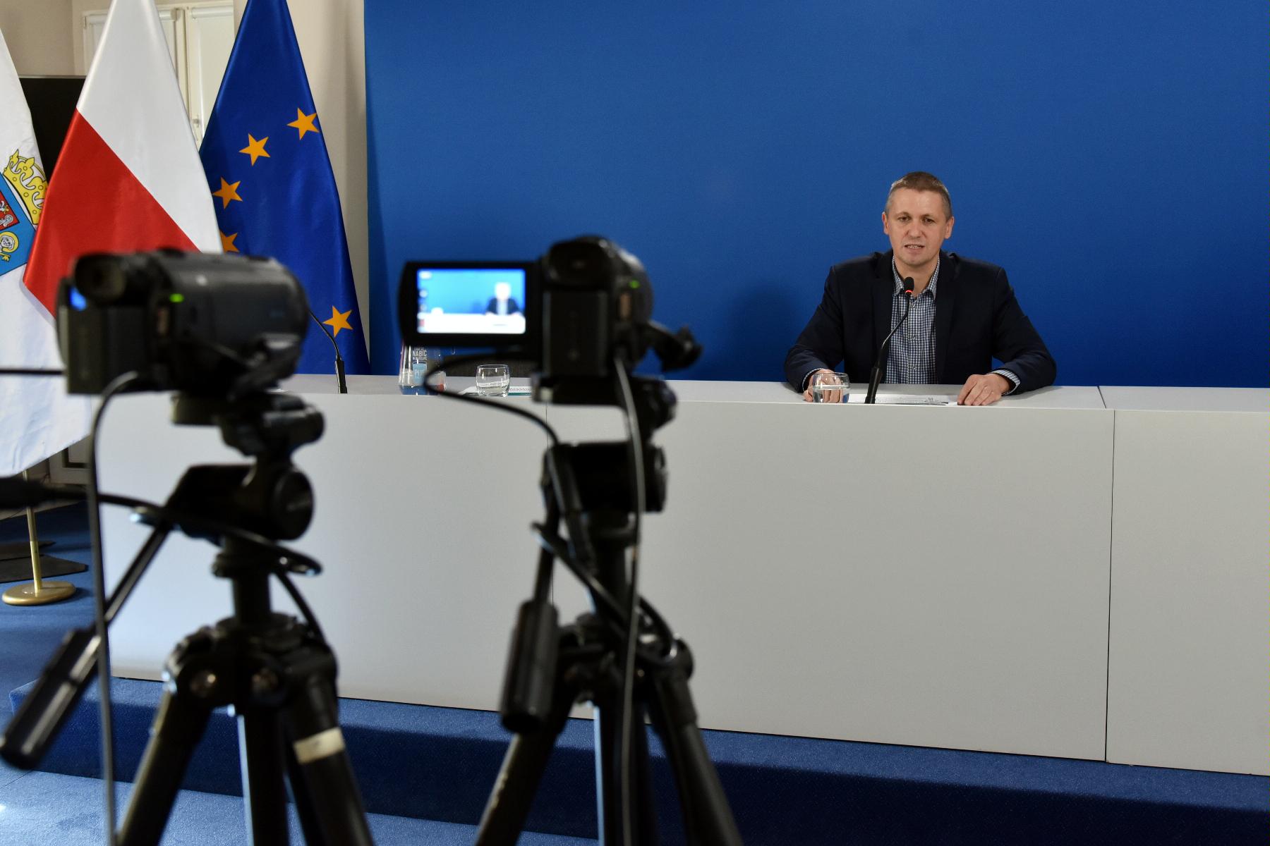 Zdjęcie przedstawia Patryka Pawełczaka, dyrektora Gabinetu Prezydenta Urzędu Miasta za stołem konferencyjnym. Na pierwszym planie widać kamery. - grafika artykułu
