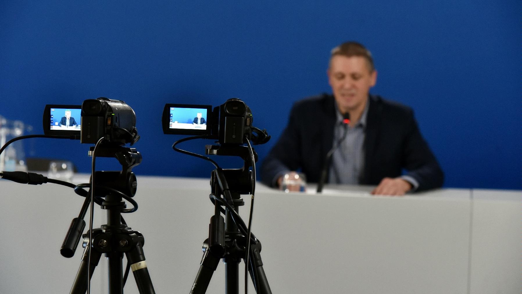 Zdjęcie przedstawia Patryka Pawełczaka, dyrektora Gabinetu Prezydenta Urzędu Miasta za stołem konferencyjnym. Na pierwszym planie widać kamery.