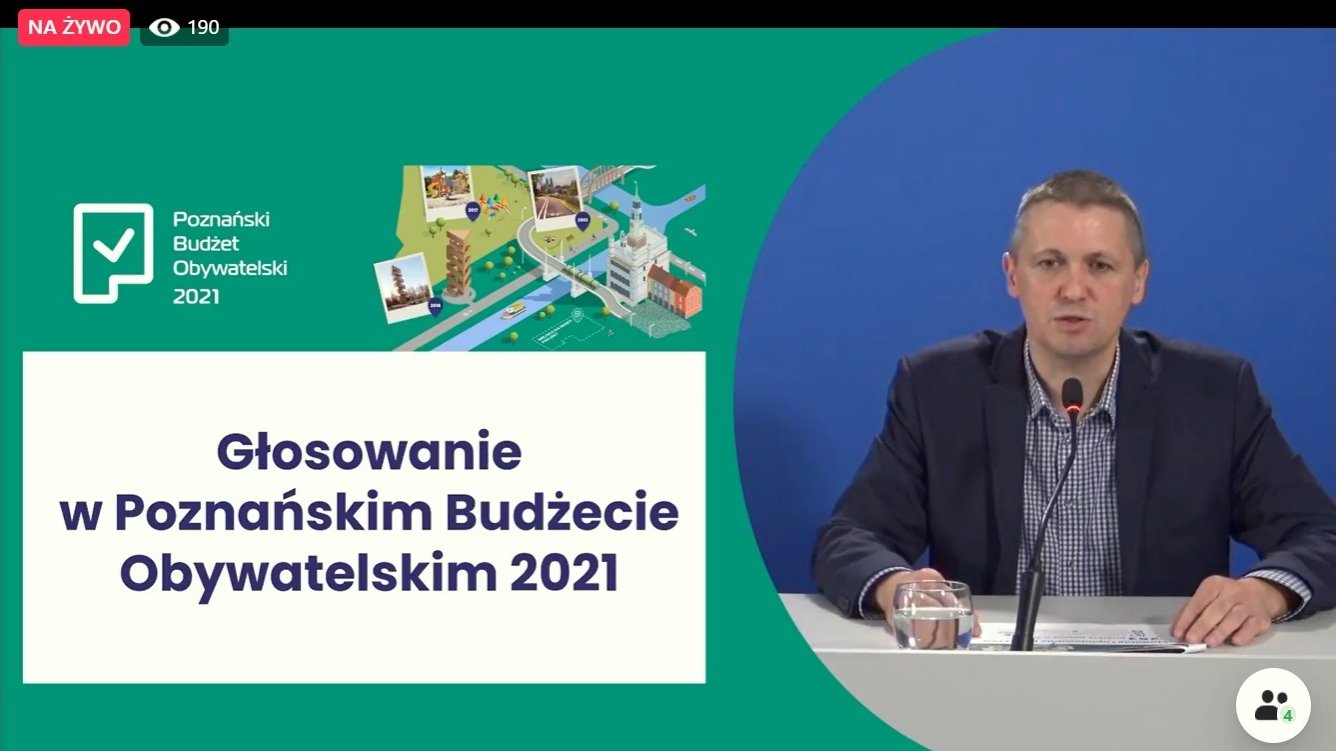 Screen z ekranu podczas transmisji. Po prawej stronie ekranu za biurkiem siedzi Patryk Pawełczak, dyrektor Gabinetu Prezydenta UMP, po lewej widać fragment prezentacji.