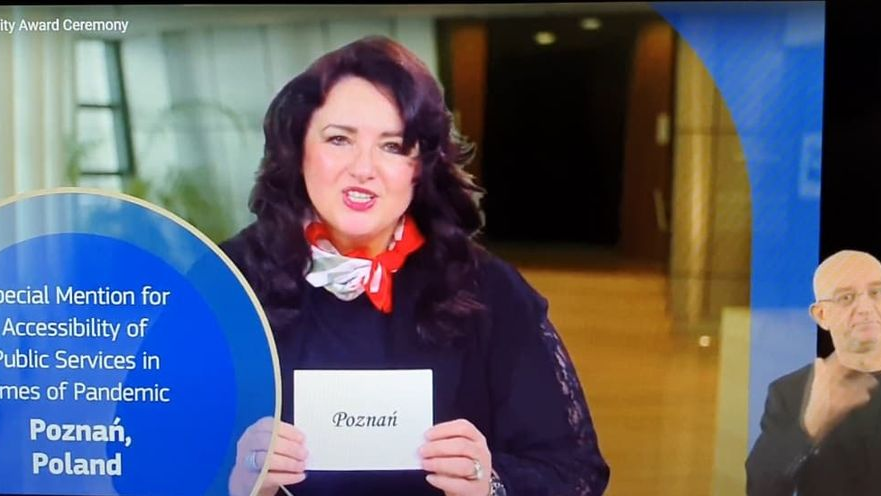 Screen: komisarz Helena Dali trzyma kartkę z nazwą zwycięskiego miasta: Poznań. Obok - tłumacz języka migowego