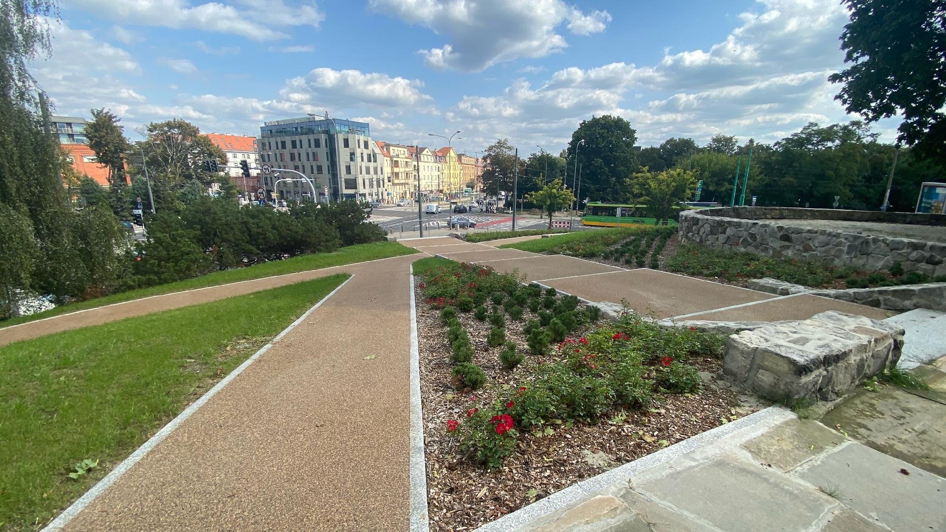 Galeria zdjęć przedstawia park Drwęskich. Na zdjęciu widać świeżo posadzoną zieleń oraz alejki spacerowe. W oddali można dostrzec ulicę.