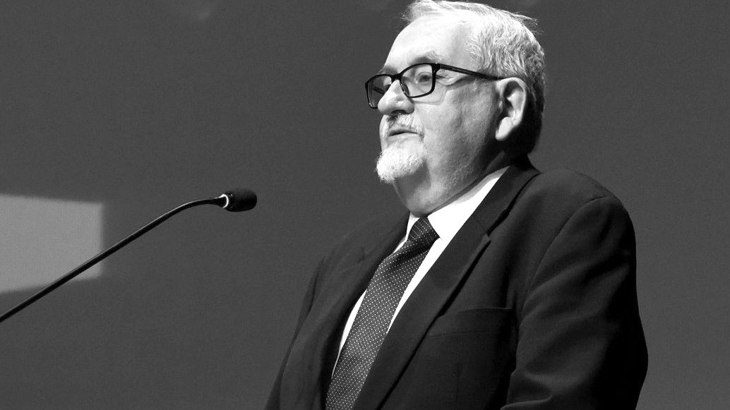 Na czarno-białym zdjęciu profesor stojący przed mikrofonem, podczas jednej z poznańskich debat