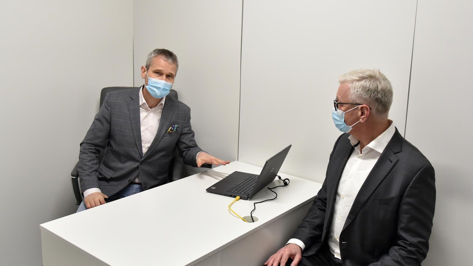 Wnętrze punktu, Jacek Jaśkowiak i Jędrzej Solarski w gabinecie medycznym, siedzą po dwóch stronach biurka, na którym stoi laptop
