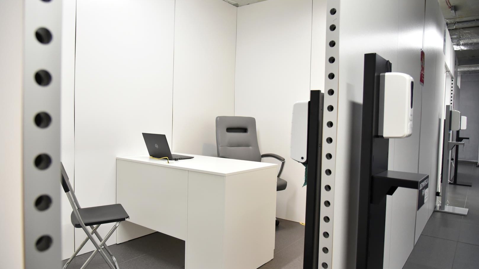 Wnętrze punktu, gabinet, w którym przeprowadzana będzie kwalifikacja: białe biurko, dwa krzesła, pojemnik z płynem do dezynfekcji