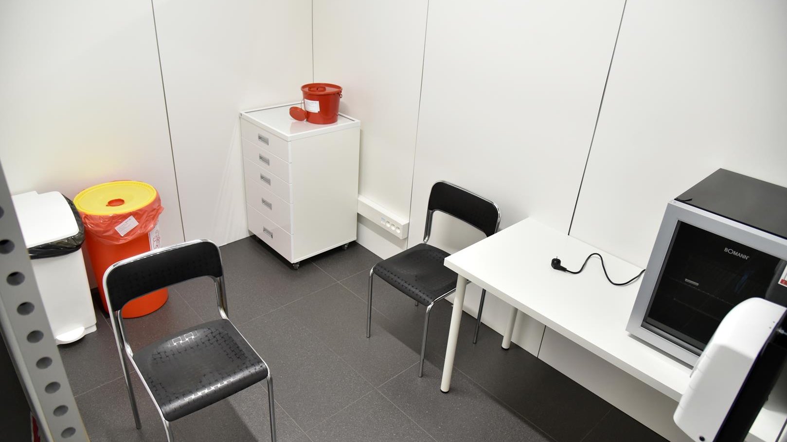Wnętrze punktu, gabinet, w którym przeprowadzane będą szczepienia: białe biurko, dwa krzesła, szafka