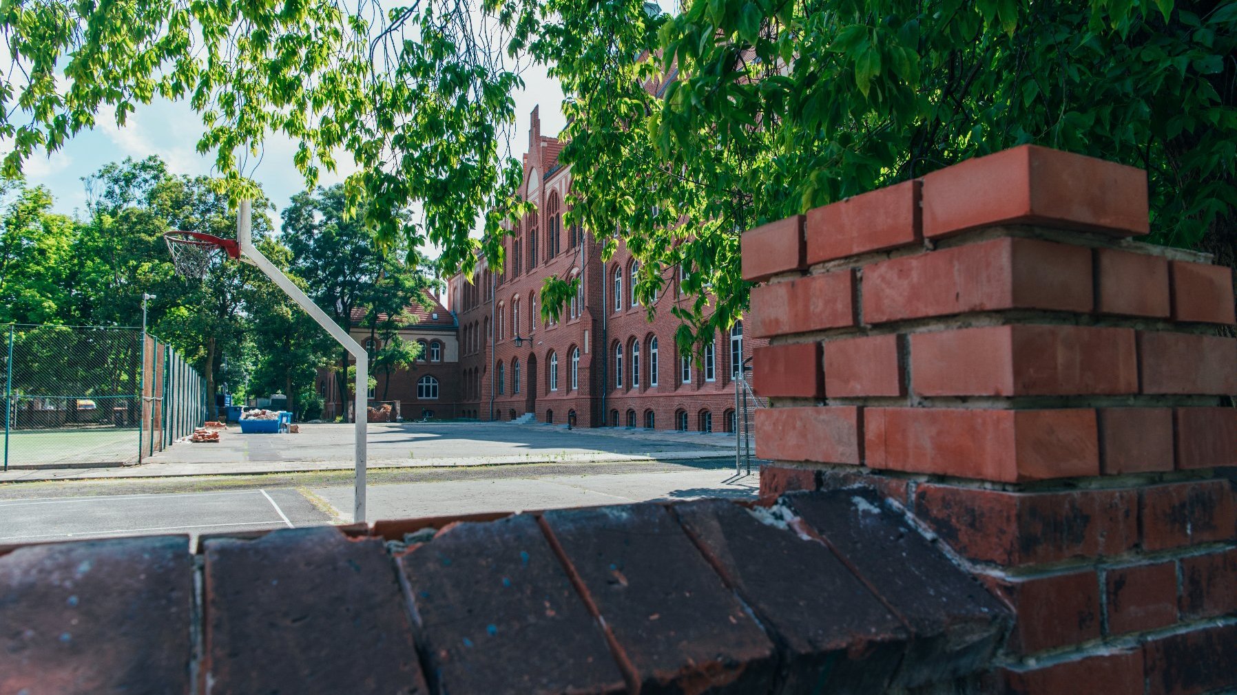 Zdjęcie przedstawia budynek szkoły, na pierwszym planie znajduje się betonowe ogrodzenie.