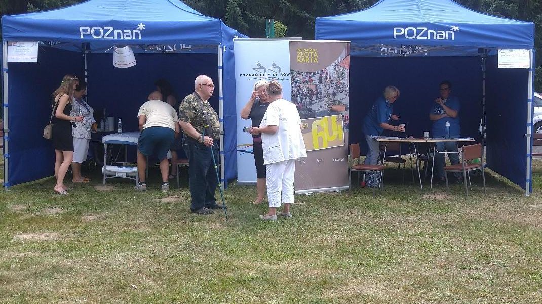 Teren ROD, dwa granatowe namioty z logotypem Miasta Poznań, przed nimi grupa starszych osób