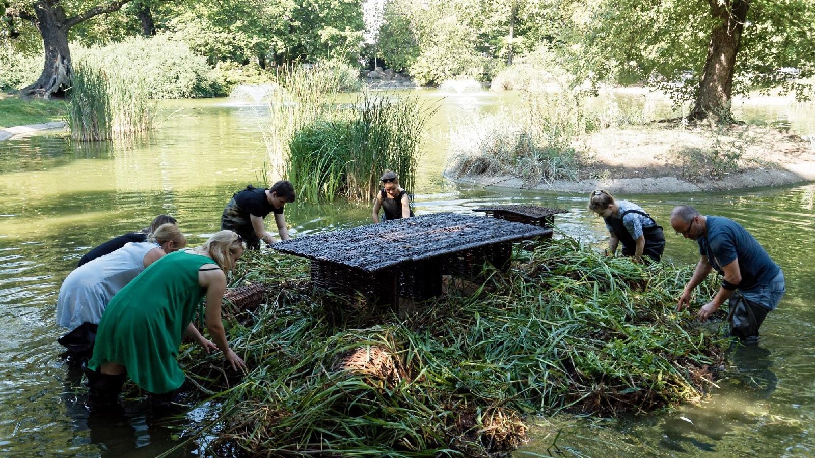 Zdjęcie przedstawia ludzi montujących pływający ogród w wodzie.