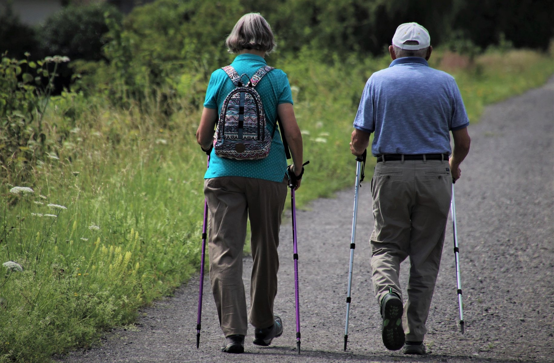 Na zdjęciu dwoje starszych ludzi, tyłem do obiektywu, maszerują z kijkami do nordic walking - grafika artykułu