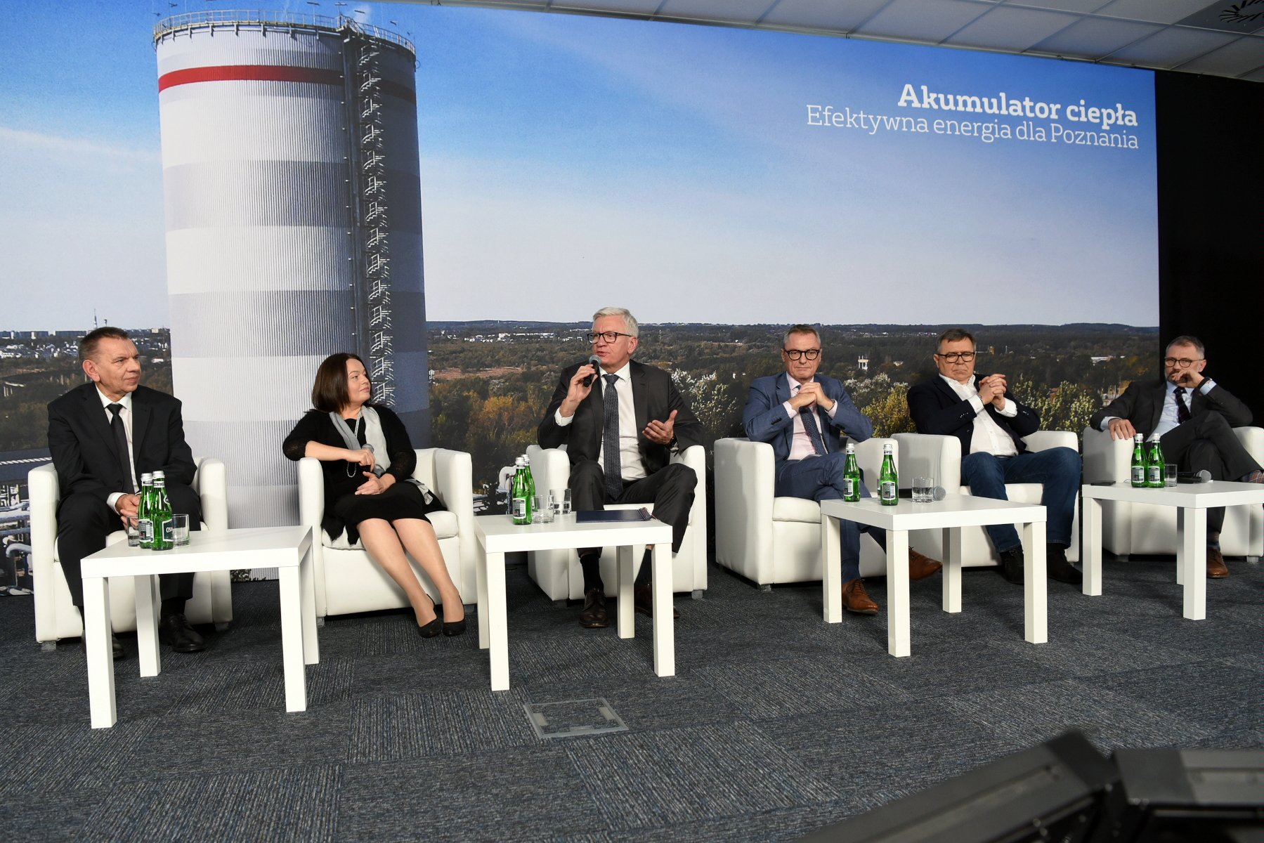 Zdjęcie przedstawia uczestników konferencji na tle zdjęcia akumulatora. - grafika artykułu