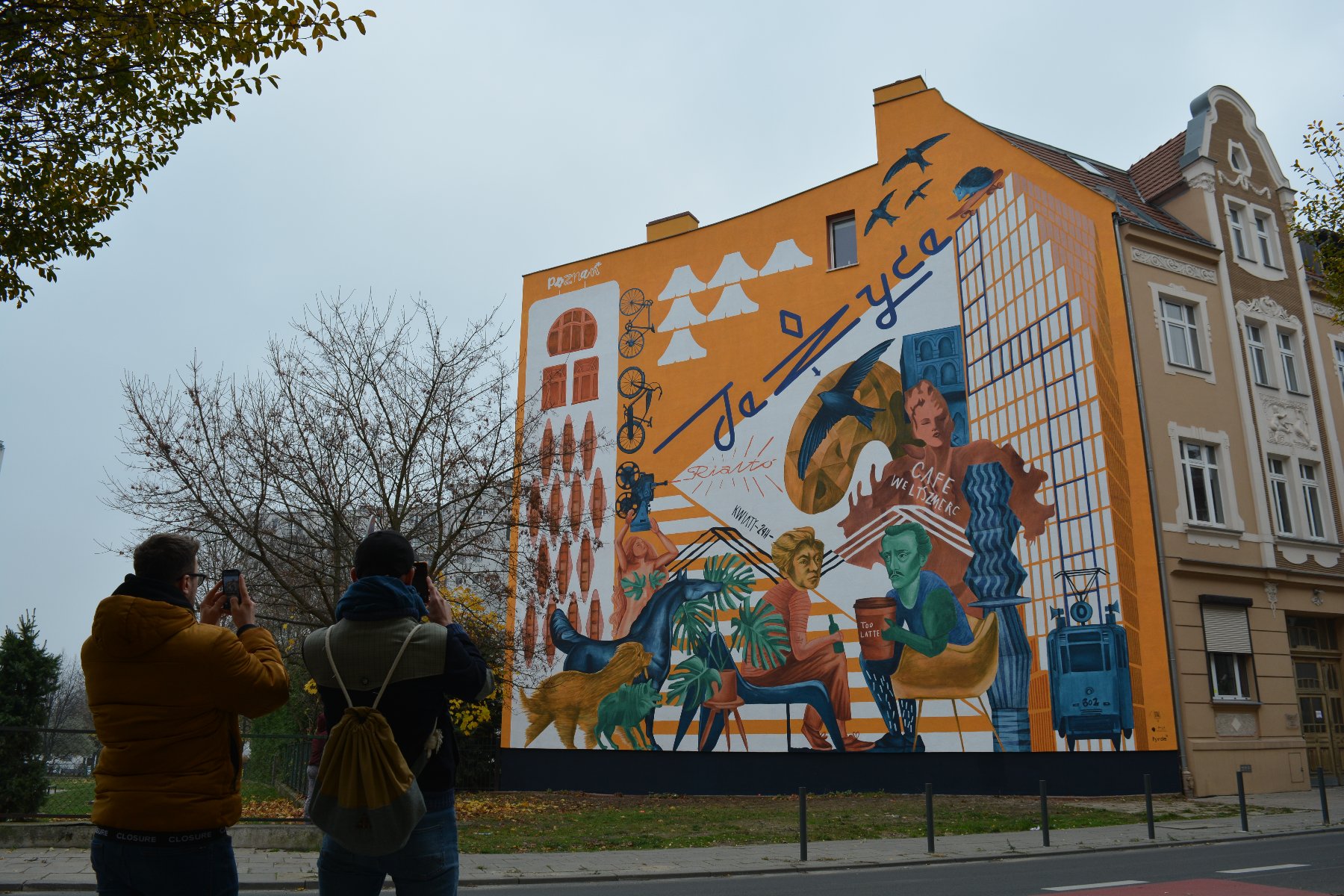 Galeria zdjęć przedstawia nowy mural na Jeżycach. Widać na nim m.in. dwóch poetów Słowackiego i Mickiewicza. Obok znajduje się ulica z samochodami. - grafika artykułu