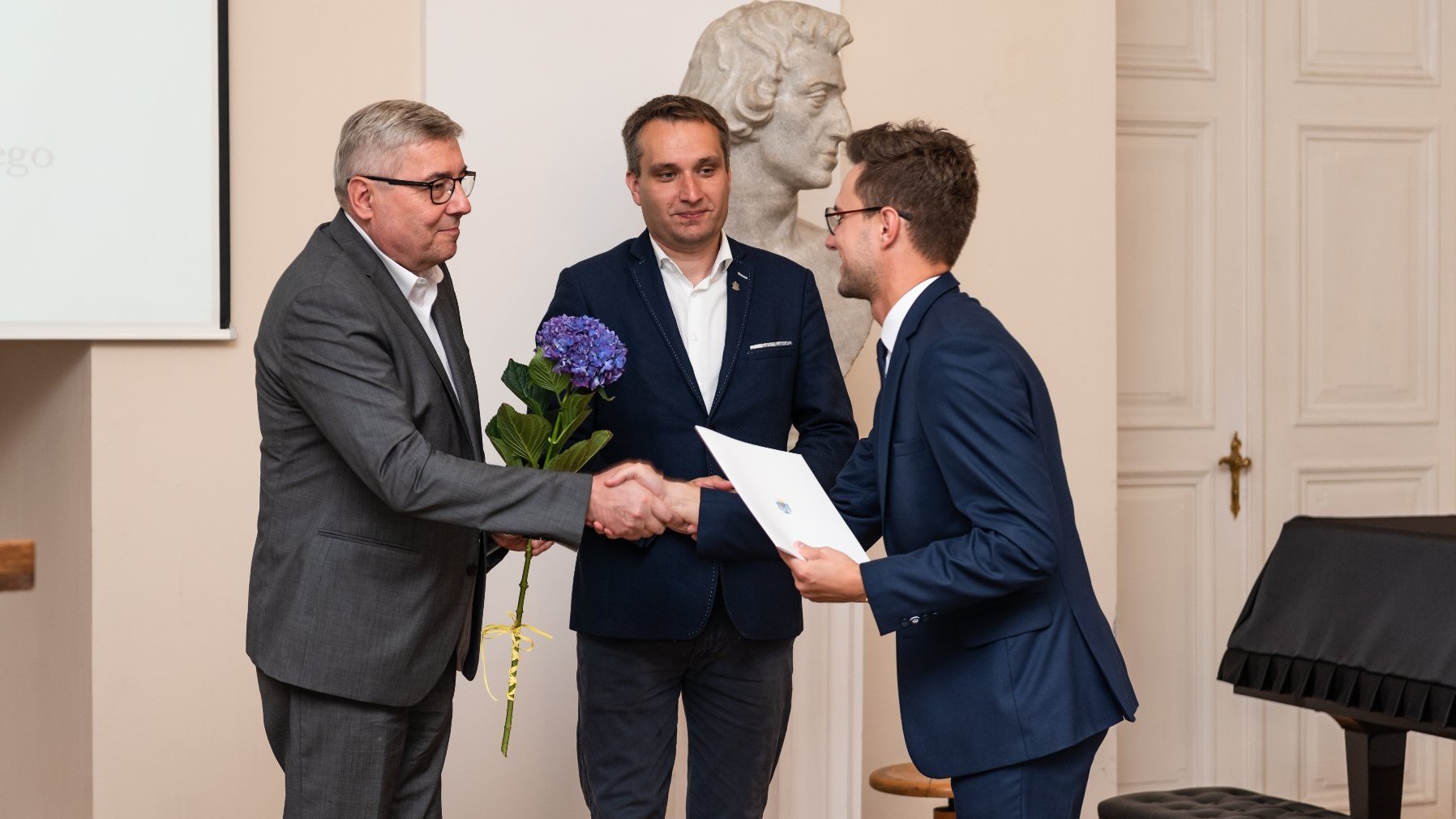 Na zdjęciu zastępca prezydenta miasta i przewodniczący rady miasta wręczają dyplom stypendyście