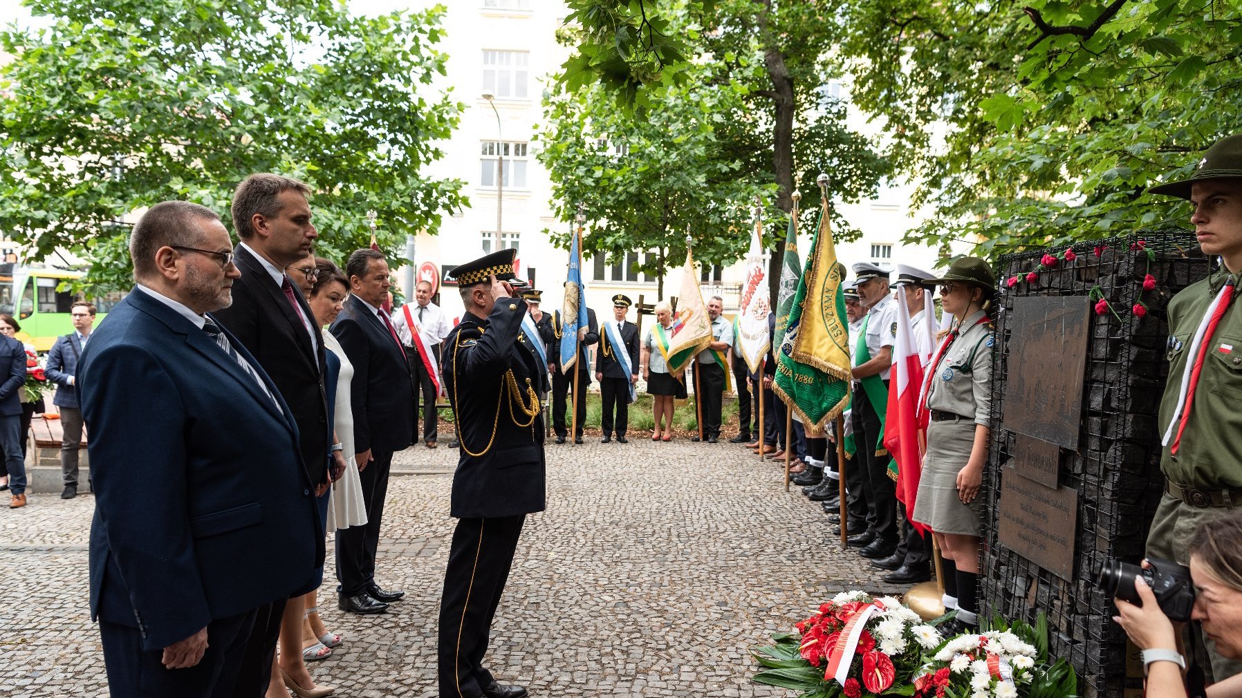 Na zdjęciu delegacja składająca kwiaty, widać tablicę, harcerzy i salutującego strażnika miejskiego