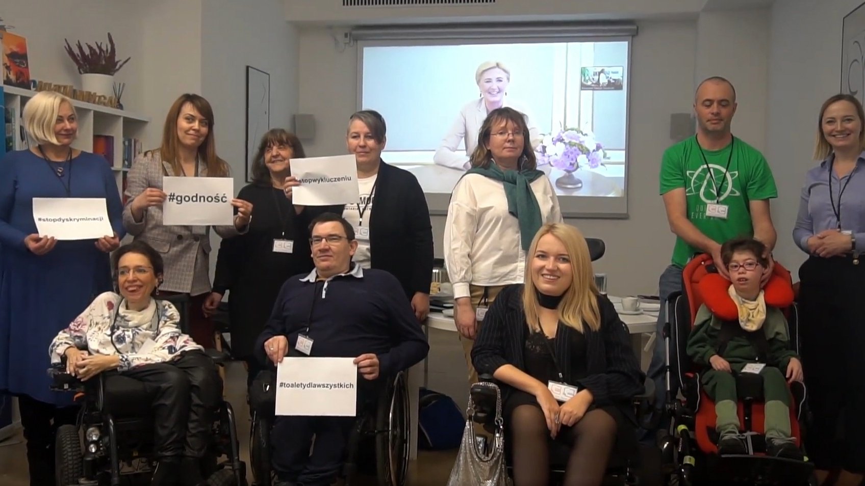 Zdjęcie przedstawia grupę osób - niektóre z niepełnosprawnościami na wózkach - pozującą do zdjęcia.