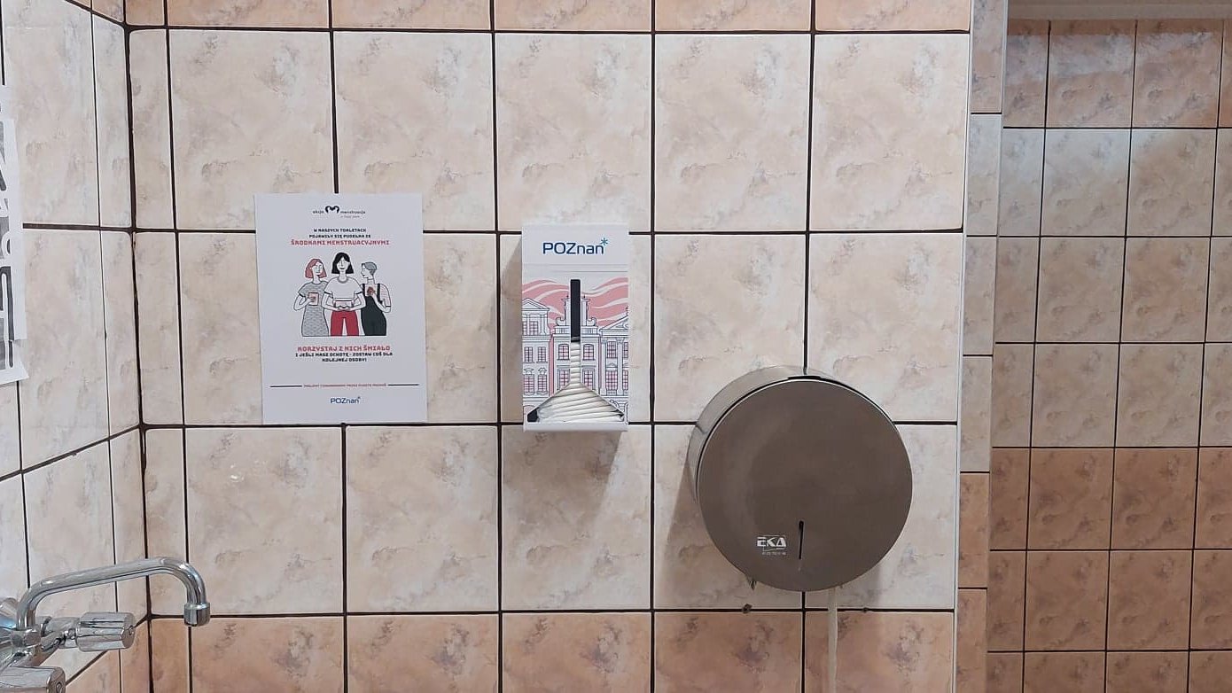 Zdjęcie przedstawia skrzynkę na środki menstruacyjne zaweszoną na ścianie toalety.
