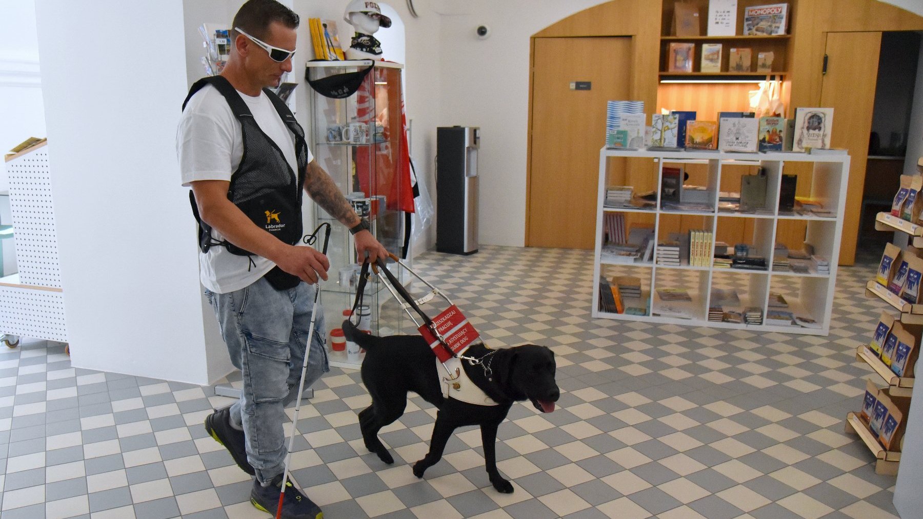 Na zdjęciu trener i pies w centrum informacji turystycznej, w tle regał z książkami