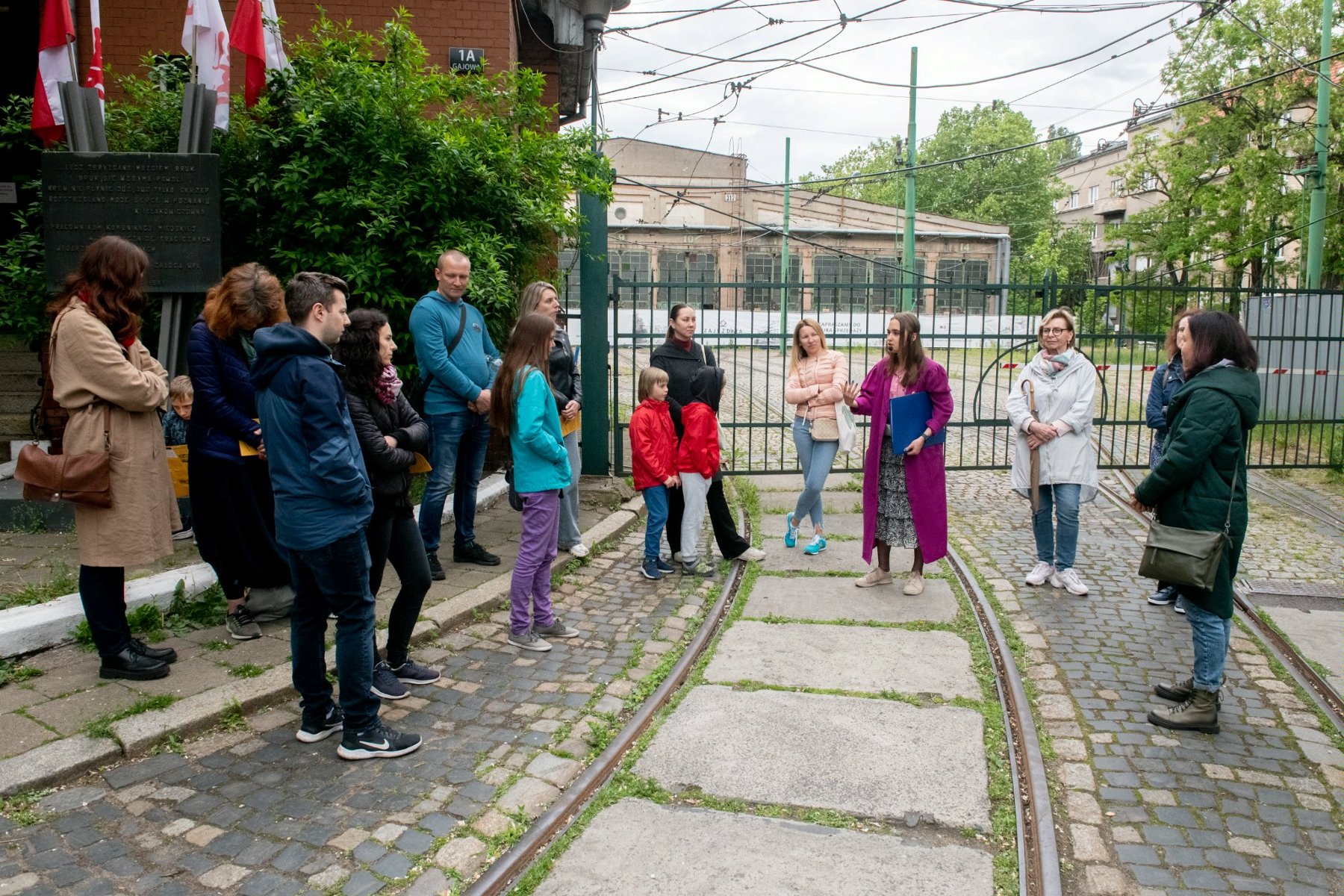 Grupa osób stoi przed zajezdnią tramwajową przy ul. Gajowej. - grafika artykułu